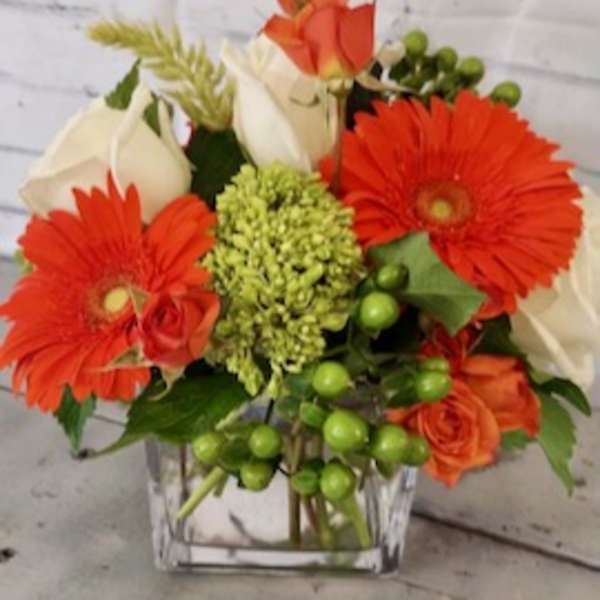 Orange gerbera daisies and white roses in a clear square vase