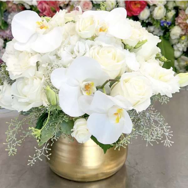 White roses and orchids arranged in a gold vase