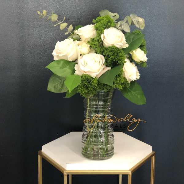 White roses arranged in a clear glass vase with green filler.