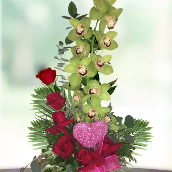 Red roses and green orchids in a vase with a pink heart pick