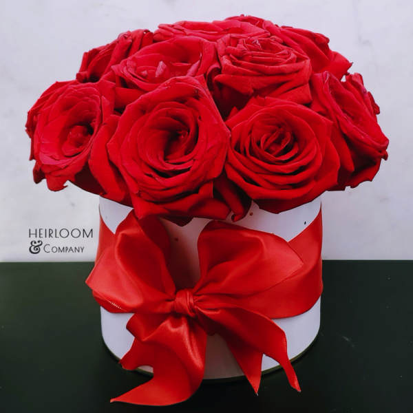 Red roses arranged in a white round box with a red ribbon bow