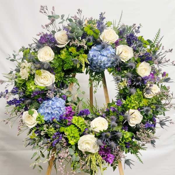 Large floral wreath with white roses, blue hydrangeas, and purple flowers