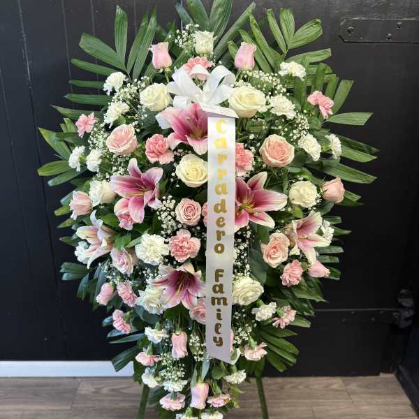Large pink and white funeral wreath on an easel with a ribbon