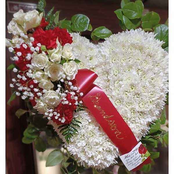Heart-shaped white and red floral arrangement with a red ribbon