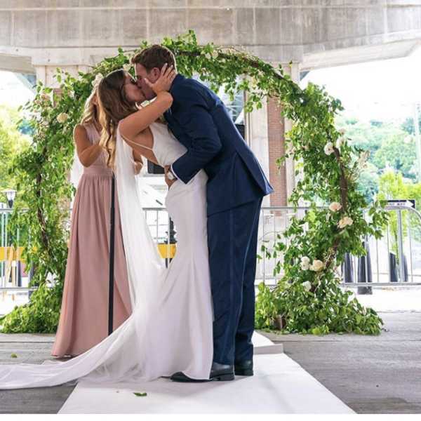 Bride and groom kissing under a greenery-covered wedding arch