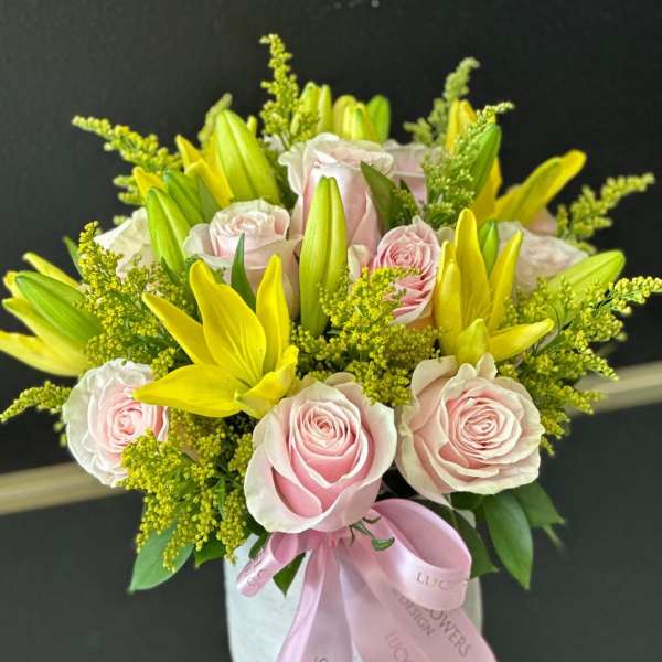 Pink roses and yellow lilies arranged in a white box with a pink ribbon