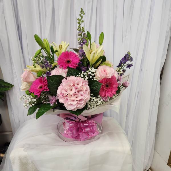 Bouquet of pink gerberas, roses, lilies, and hydrangea in a clear vase