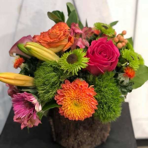 Colorful mixed bouquet with roses, lilies, and chrysanthemums in a rustic container
