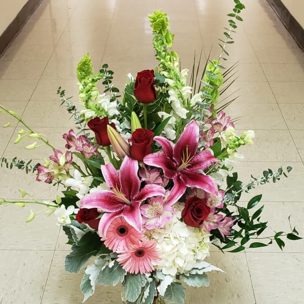 Tall bouquet of pink lilies, red roses, and white blooms in a glass vase