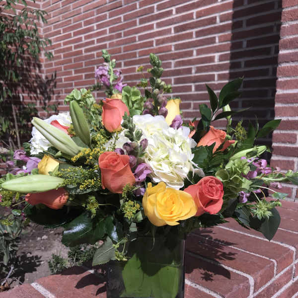 Mixed bouquet of roses, lilies, and hydrangea in a square glass vase