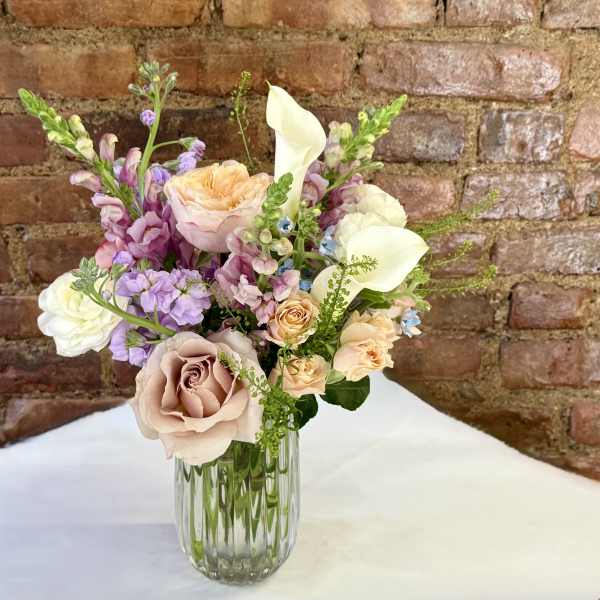 Pastel bouquet of roses, calla lilies, and purple blooms in a glass vase