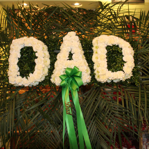 White floral letters spelling DAD with a green ribbon bow