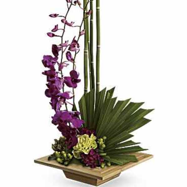 Tall floral arrangement with purple orchids and bamboo in a wooden base