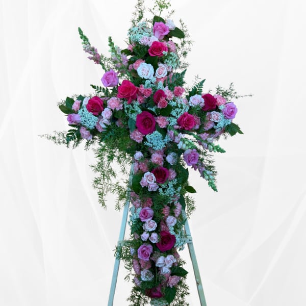 Tall floral cross covered in pink and white roses with greenery