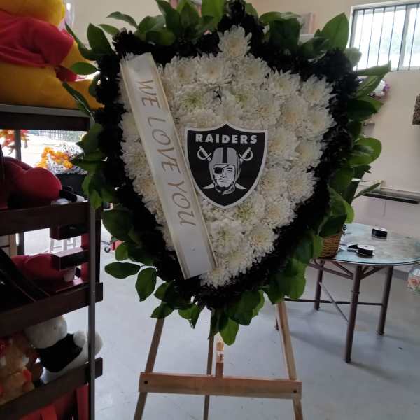 Heart-shaped white floral tribute on an easel with a Raiders emblem and ribbon