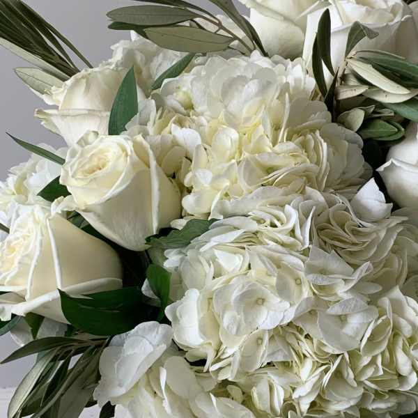 Close-up of ivory roses and white hydrangeas clustered in a lush bouquet