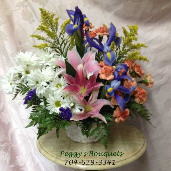 Mixed bouquet with pink lilies, blue irises, and white daisies in a basket
