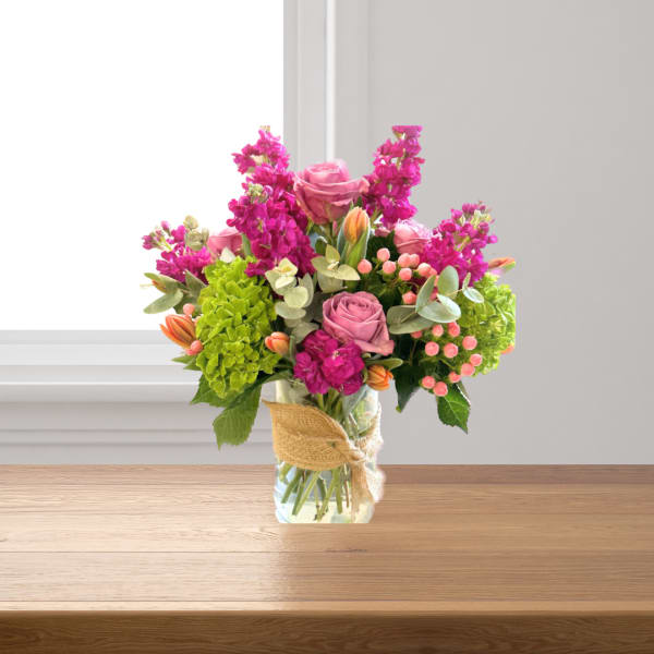 Pink roses and magenta flowers in a glass vase with burlap ribbon