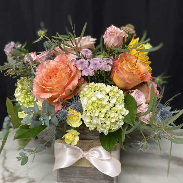 Mixed bouquet of peach roses, hydrangea, and yellow blooms in a wooden box