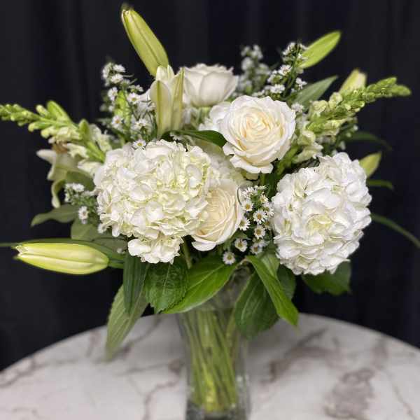 White roses and hydrangeas in a glass vase with lily buds