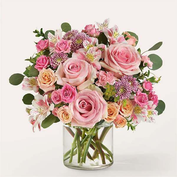 Pink roses and mixed blooms arranged in a clear glass vase