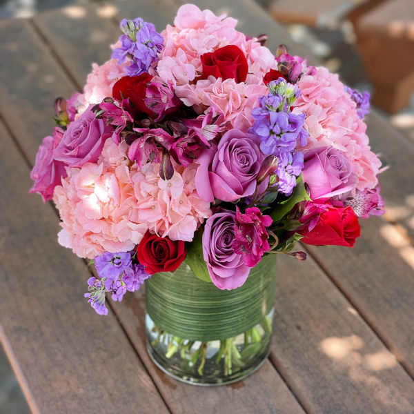 Pink and purple bouquet in a glass vase with red roses