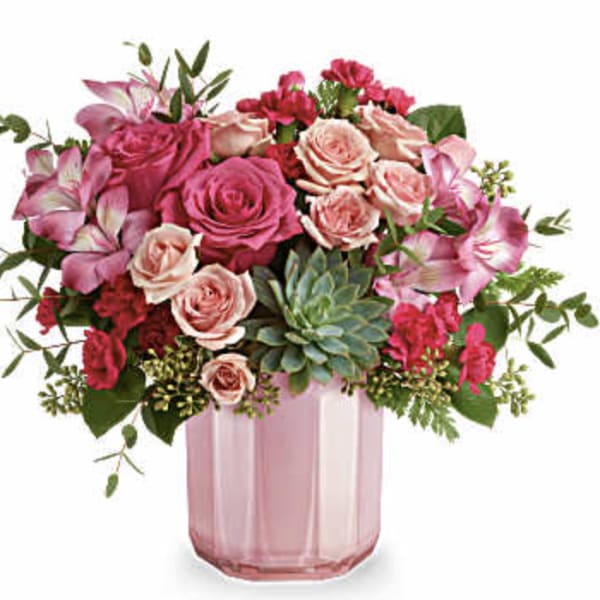 Pink and peach roses in a pink glass vase with greenery