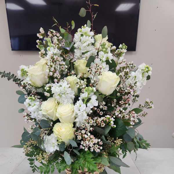 Tall basket arrangement of white roses and white blooms with small blush accents