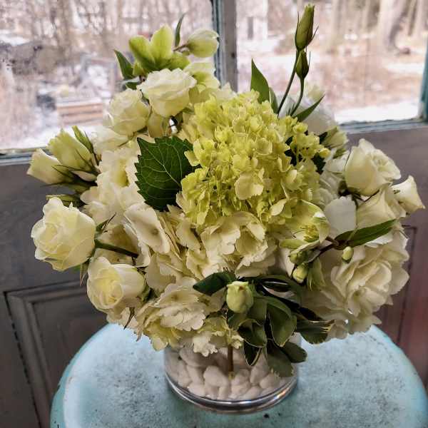White roses and hydrangeas in a clear glass vase with white stones