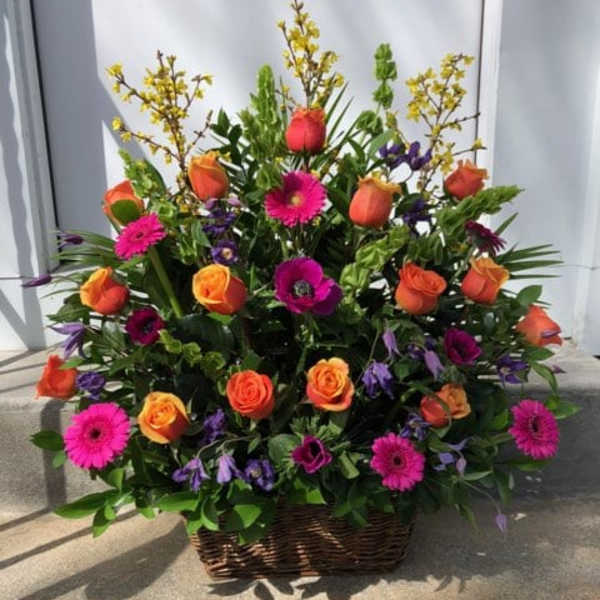 Basket arrangement of orange roses, pink gerberas, and purple flowers