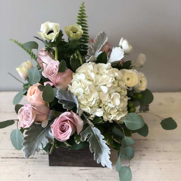 Low arrangement of white hydrangea, pale pink roses, and white blooms in a wooden box.