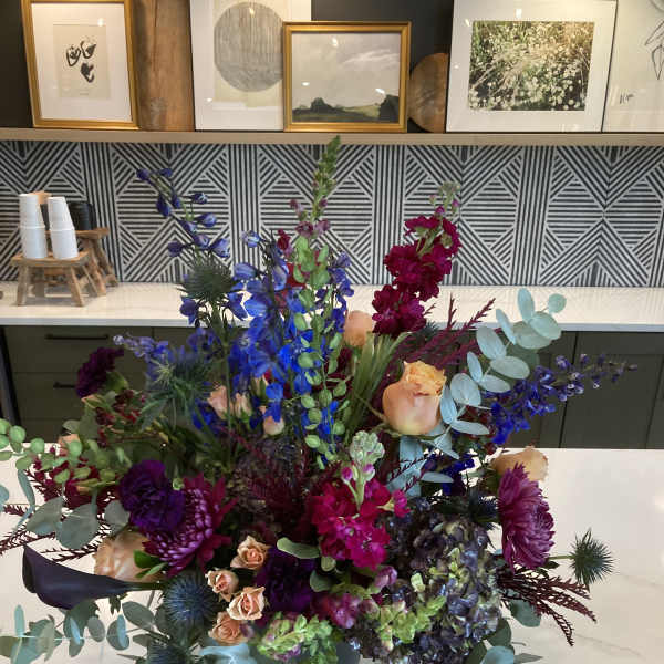 Large mixed floral arrangement in a dark vase with blue, purple, and peach blooms