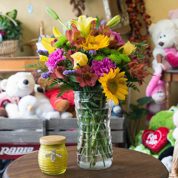 Mixed bouquet of yellow, pink, and purple flowers in a clear glass vase