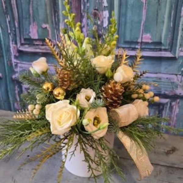 Cream roses and white blooms arranged in a white vase with pinecones