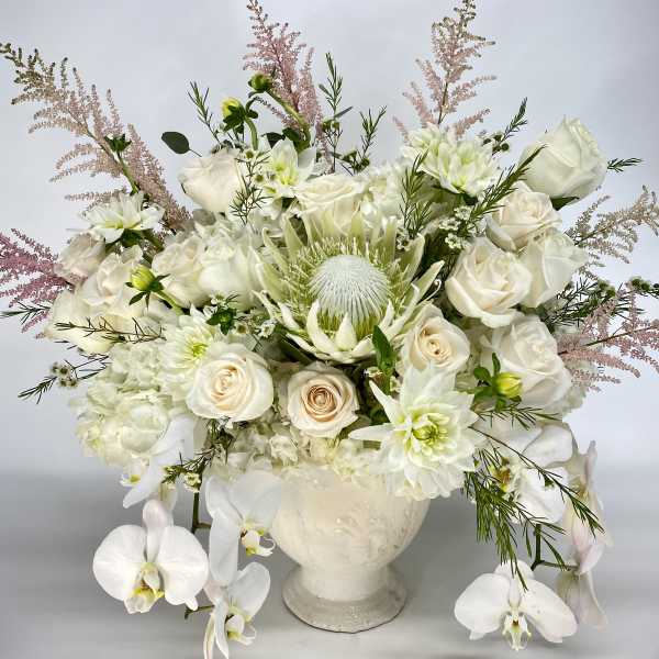 White floral arrangement in a cream vase with roses and orchids