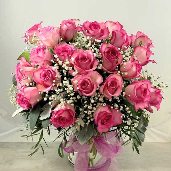 Pink roses arranged in a glass vase with baby's breath and ribbon