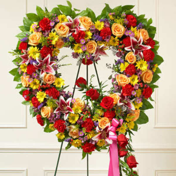 Heart-shaped floral wreath on a stand with roses, lilies, and mixed blooms