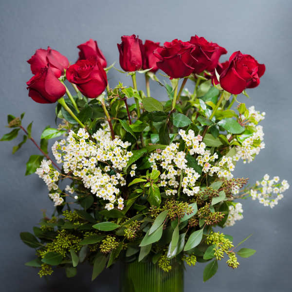 Red roses arranged in a green glass vase with white filler flowers