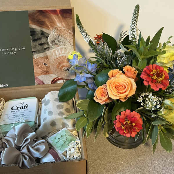 Gift box with flowers, a cocktail kit, and accessories beside a colorful bouquet