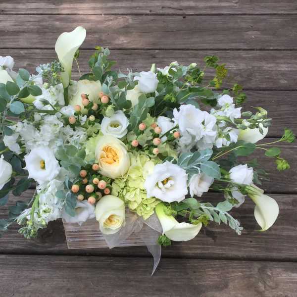 White floral arrangement with calla lilies, roses, and lisianthus in a clear container