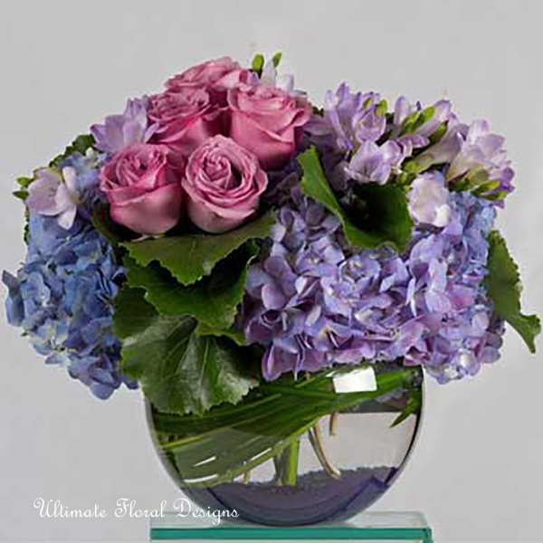 Pink roses and purple hydrangeas arranged in a clear glass vase