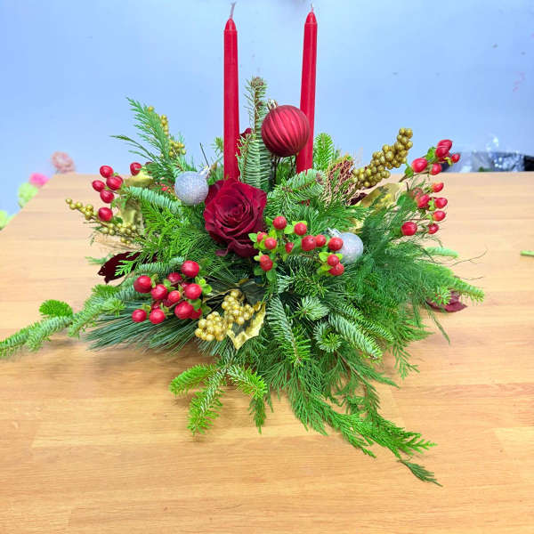 Holiday centerpiece with red candles, a red rose, and evergreen branches