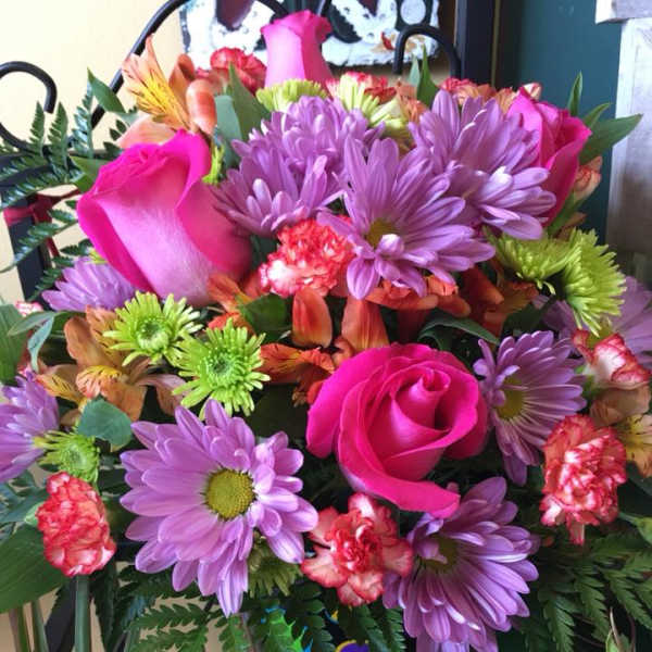 Bouquet of pink roses, purple daisies, and mixed blooms in a decorated vase