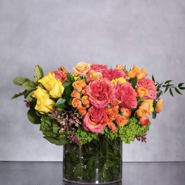 Mixed bouquet of pink, yellow, and orange roses in a glass vase
