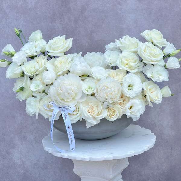 White roses and lisianthus arranged in a gray bowl on a pedestal