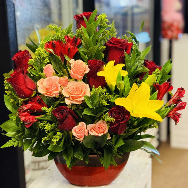 Red and peach roses with yellow lilies in a red vase