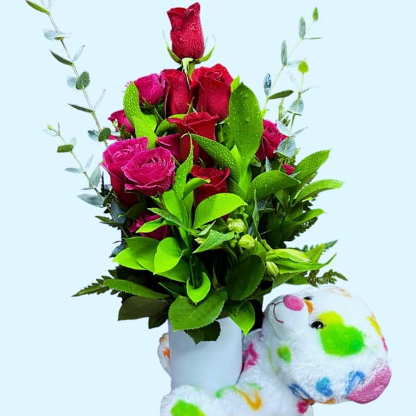 Bouquet of red roses in a white vase with a colorful teddy bear