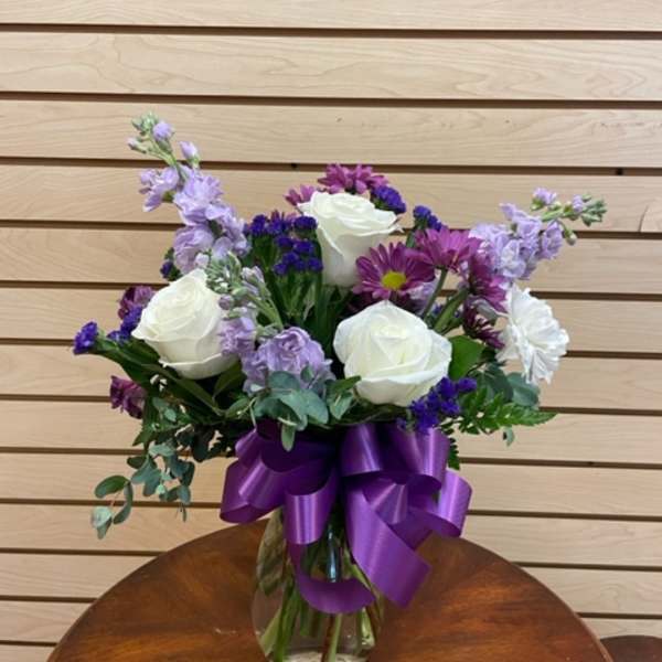 Bouquet of white roses and purple flowers in a glass vase with a purple ribbon