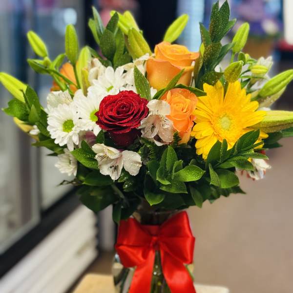 Bouquet of roses, daisies, and lilies in a glass vase with a red ribbon