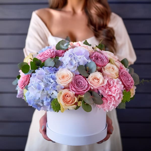 Woman holding a round box of pastel roses and hydrangeas